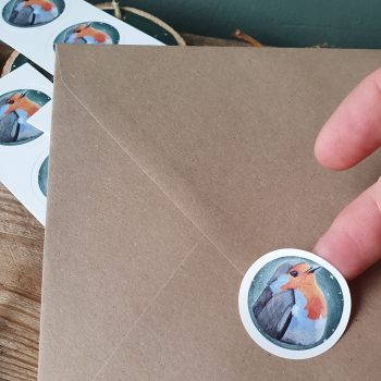 Een ronde sticker met roodborstje wordt op een envelop geplakt.